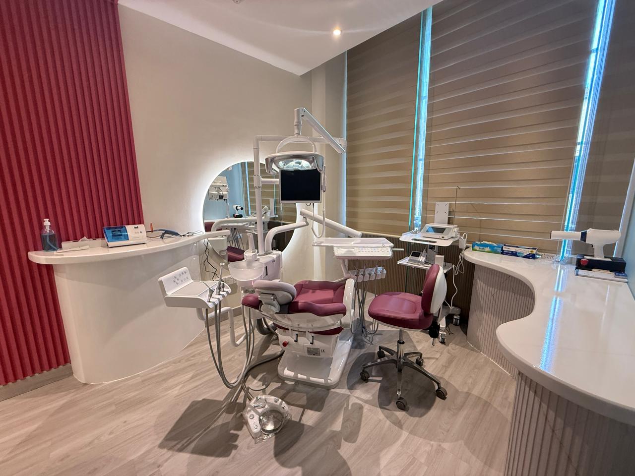 Bright dental treatment room with a burgundy chair and clinical equipment
